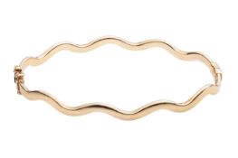 A hinged oval bangle of undulating design, with tongue clasp and safety catch, in polished yellow me