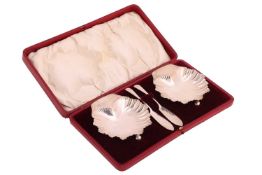 A pair of silver shell butter dishes and knives, of fluted shell form on three ball feet, London 191