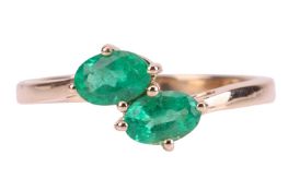 An emerald-set crossover-style ring, with two oval mixed-cut emeralds, claw-set in a 9ct yellow gold