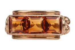 A citrine three-stone dress ring, channel-set with three square table-cut citrines, between volute s