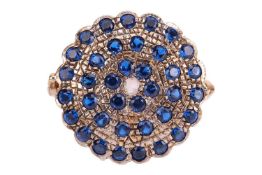 A gem-set circular ring, featuring a rose-cut diamond to the centre, surrounded by three rows of blu