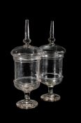 A PAIR OF CLEAR GLASS PEDESTAL CHEMIST JARS AND COVERS