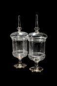 A PAIR OF CLEAR GLASS PEDESTAL CHEMIST JARS AND COVERS