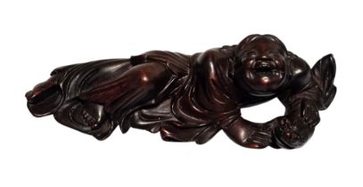 A Japanese carved hardwood okimono of Hotei, the Laughing Buddha, depicted reclining in flowing