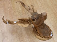 An ornate hand carved head of a deer fixed to a wall hanging plaque.