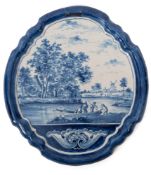 A Delft wall plaque, c.1900, painted in blue with figures in and beside a fishing boat on a river, w