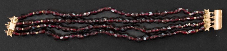 Jewellery: a yellow metal mounted garnet four strand bracelet, the clasp set with three further cabo