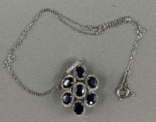 Jewellery: White metal, 36cm chain with an oval pendant attached, set with seven oval-cut sapphires,