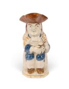 A Pratt ware Toby jug, c.1800, of Ordinary type, wearing a patterned coat over blue breeches, his sm