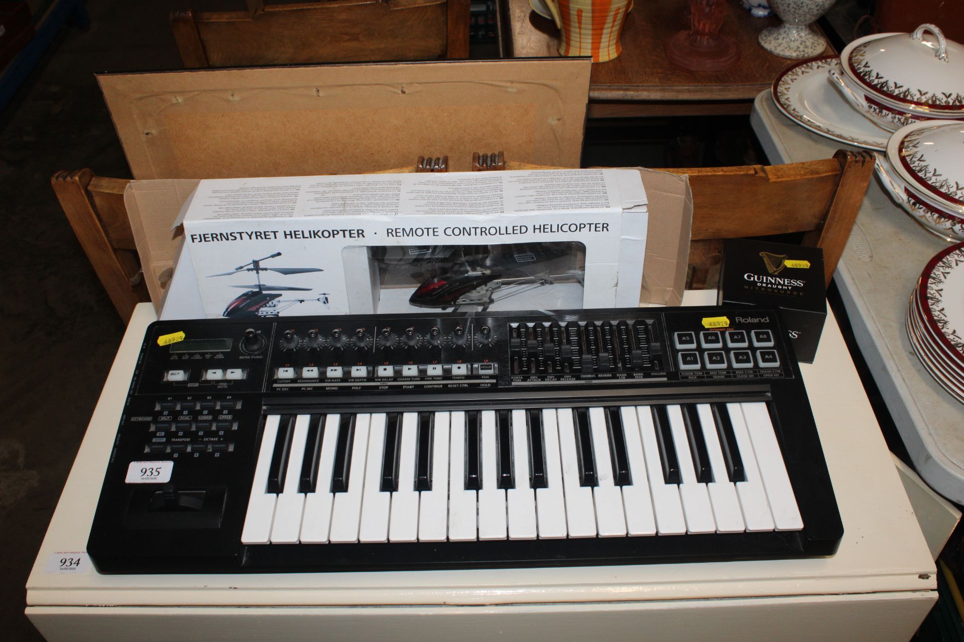 A Roland keyboard lacking power lead together with a remote controlled helicopter and a Guinness