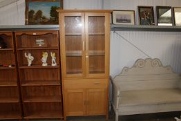 A modern light oak display cabinet raised on cupbo