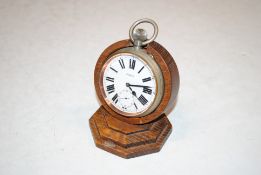 A eight day silver plated pocket watch, 7cm dia. on wooden stand