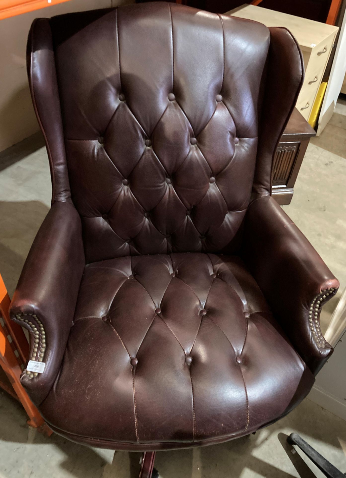 A brown leather high deep buttoned back and seat swivel armchair - please note: slight tear to arms,