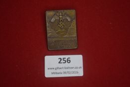 German political badge, rectangular form depicting eagle and swastika above landscape scene, with