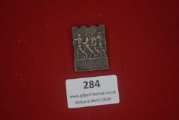 German Third Reich period tinnie, cast metal example depicting marching figures, titled “