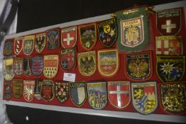 A large collection of embroidered souvenir and heraldic cloth badges, predominantly shield-shaped,