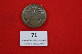 German circular alloy badge with stylised radiating motif and script inscription, marked BDF to