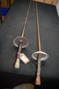 Pair of fencing foils, each with slender straight blade and circular bell guard,