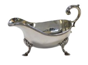 A late Victorian silver sauce boat, with an open acanthus handle and beadwork border, raised on