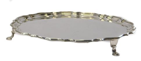 A George V silver salver, of circular form with a piecrust border, raised on three hoof feet,