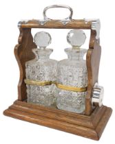 An early 20thC oak and silver mounted twin division tantalus, containing two cut glass square