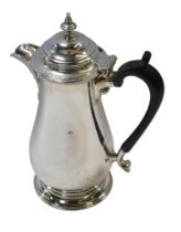 A George V silver hot water jug, of baluster form, with an ebonised handle, raised on a circular