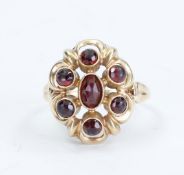 Yellow gold entourage ring, 14kt, set with a garnet in a floral design, Dutch hallmarked, 3 grams.
