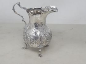A Victorian silver Jug embossed floral swags and ribbons, engraved crest, shaped rim on three scroll