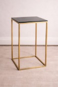 A polished brass tall side table featuring a square, black tempered glass top inset within a slender