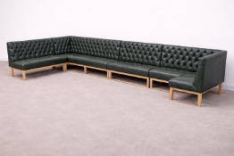 A large modular sectional banquet sofa upholstered in dark green leather, featuring extensive deep-