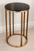 A tall circular side table featuring a black tempered glass top inset within a brushed brass-