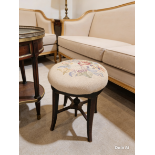A revolving piano stool in a traditional style, featuring a circular seat upholstered in cream