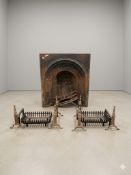 A Victorian cast iron arched fireplace insert alongside a pair of contemporary fire baskets and fire