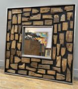 A modern metal-framed wall mirror, central square plate surrounded by wood fragments, enclosed