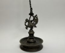An Indian brass oil lamp with peacock finial above a circular base with chain and hook of serpent