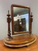 An Edwardian mahogany swing mirror, rectangular plate raised on decorative supports and carved