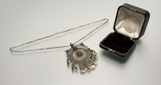 An Iranian brass circualr pendant with inset glass jewel floral bead design and fringed on chain