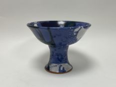 A large studio pottery pedestal bowl, decorated with shades of green and blue drip glazed over a