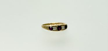 An Edwardian yellow metal ring set three graduated round facet-cut rubies, centre stone