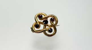 An Edwardian 9ct gold Celtic style knot brooch set five cognac coloured round faceted garnets with