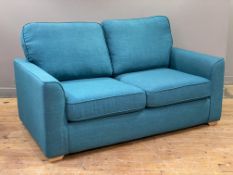 A modern two-seater sofa bed, upholstered in teal fabric with loose back and seat cushions, with