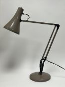 An Anglepoise lamp in a light beige colourway of typical hinged and rotating form on a weighted
