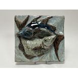 A stoneware plaque modeled with two fish in high relief, glazed in blue, orange, and green tones,