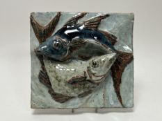 A stoneware plaque modeled with two fish in high relief, glazed in blue, orange, and green tones,