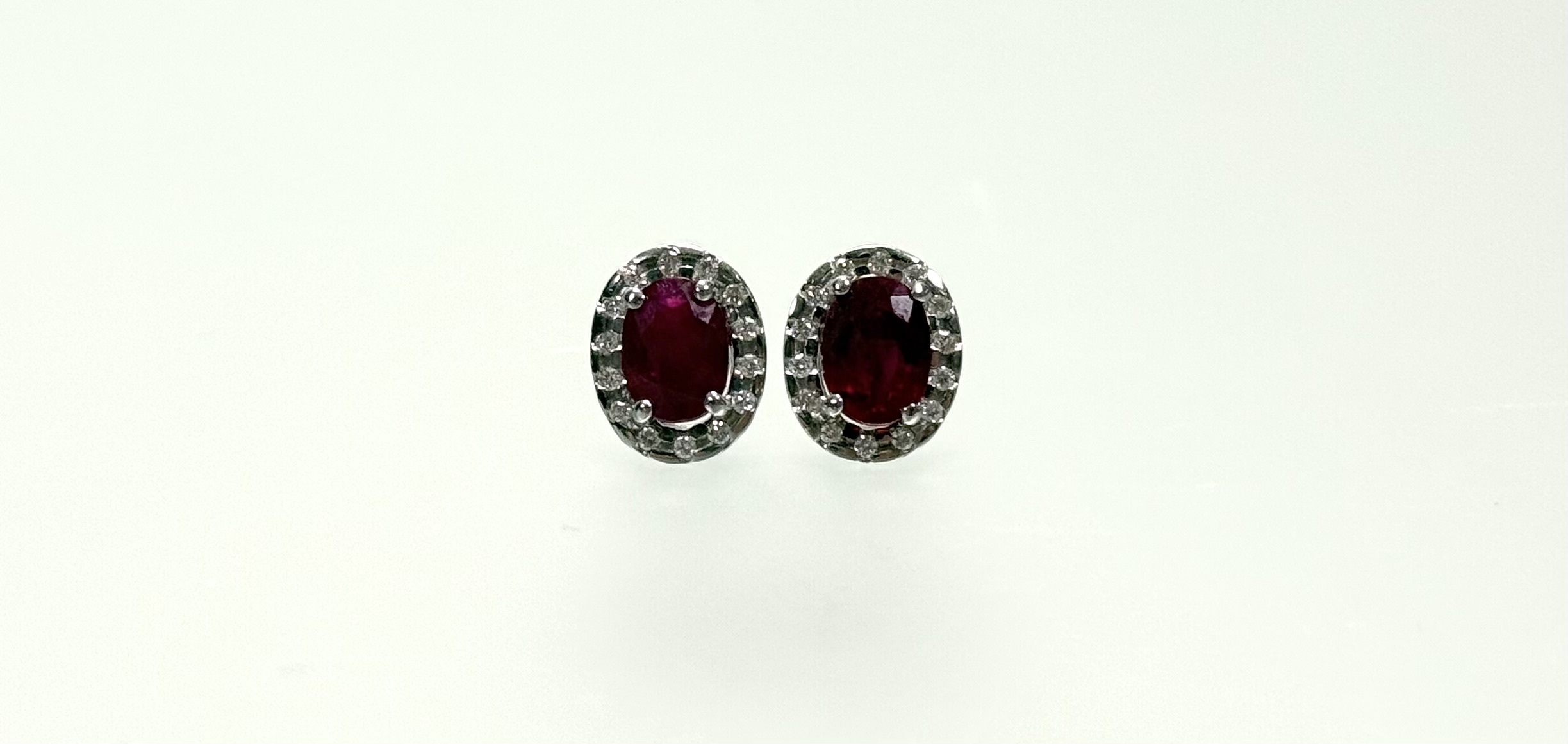 A pair of ruby and diamond cluster earrings set in 18ct white gold, each with an oval-cut ruby