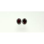 A pair of ruby and diamond cluster earrings set in 18ct white gold, each with an oval-cut ruby