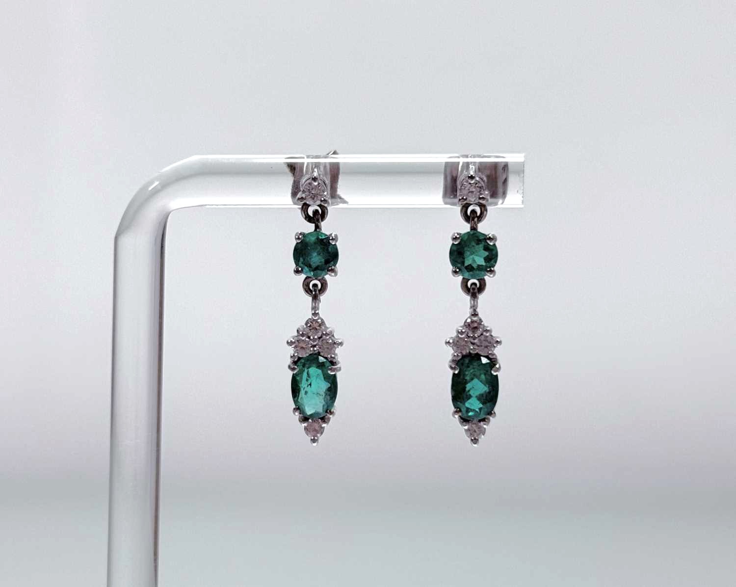 A pair of 9ct white gold pendent earrings each set with an oval emerald (enhanced) of