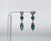 A pair of 9ct white gold pendent earrings each set with an oval emerald (enhanced) of