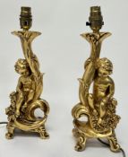 A pair of gilt resin table lamps, modelled as putti on naturalistic bases, complete with cream