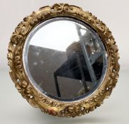 A late 20thc oval table mirror with a foliate scrolling gilt wood frame and bevelled mirror panel